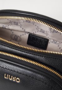 Interno di una borsa in pelle nera con dettagli della cerniera dorata, caratterizzato da un'etichetta texturizzata e una fodera beige a fantasia con loghi e forme geometriche.
