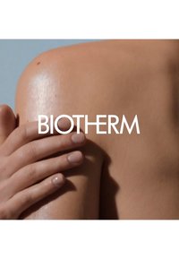Produit Biotherm mettant en avant une main sur une épaule lisse et légèrement brillante. Le ton de la peau est moyen avec des détails subtils comme des taches de rousseur.