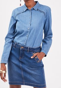 Koszula dżinsowa z guzikami z przodu, kołnierzykiem i falbanami. Połączona z dżinsową spódnicą z przednimi kieszeniami i brązowymi akcentami.