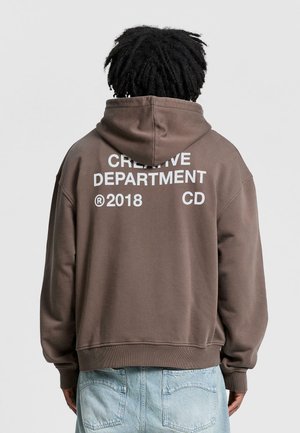 Brauner Kapuzensweatshirt mit großem weißen Textdruck auf der Rückseite: "KREATIVABTEILUNG 2018 CD." Hergestellt aus weichem Material, normale Passform.