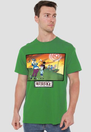 Man wearing green t-shirt with colorful Beetlejuice cartoon scene showing two main characters and a sunset background.