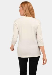 Witte top met driekwartmouwen en een ronde halslijn, met een gladde textuur, gezien vanuit de achterkant. Gecombineerd met zwarte broek.