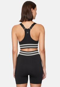 Svart sportbehå och högmidjade shorts med vita ränder. Behån har en racerback-design och justerbara remmar. Strukturerad material.