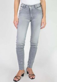 Jean slim fit taille haute en denim gris clair, avec poches avant et fermeture éclair, associés à des sandales à talons noires.