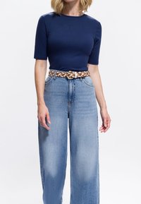 Marineblaue eng anliegende T-Shirt mit kurzen Ärmeln, kombiniert mit hellblauen Jeans mit weitem Bein und einem geflochtenen braun-weißen Gürtel mit goldener Schnalle.