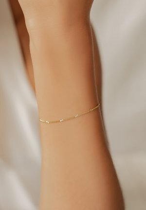 Goldene Kettenarmband an einem Handgelenk, das kleine, klare Steine enthält, die gleichmäßig in das zarte, gedrehte Design eingesetzt sind. Glatte Hautfarbe.