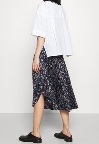 Valkoinen ylisuurikokoinen paita yhdistettynä laskostettuun, tummakukkaiseen hameeseen, jossa on sinisen ja harmaan vivahteita, sekä mustiin liukuviin kenkiin.