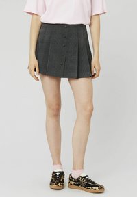 Jupe à carreaux gris avec des plis et une fermeture à boutons sur le devant. Associée à un haut rose et des baskets noires avec un motif léopard.