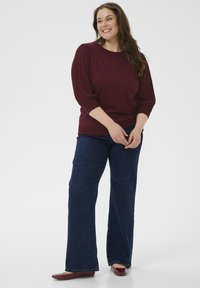 Pull en maille bordeaux avec des manches bouffantes, associé à un jean évasé bleu foncé et des ballerines bordeaux, présentant une texture lisse et un design décontracté.