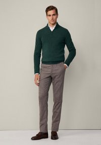 Grüner Zip-Pullover aus strukturiertem Stoff, kombiniert mit hellbraunen, strukturierten Hosen und dunkelbraunen Mokassins. Einfaches, klassisches Design.