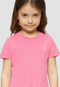 Rosa Baumwoll-T-Shirt mit kurzen Ärmeln, gewelltem Ausschnitt und einem erhöhten Herzmotiv auf der linken Brust. Weicher Stoff.