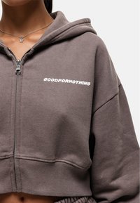 Grijze cropped hoodie met een rits aan de voorkant, met "GOODFORNOTHING" in witte tekst. Gemaakt van een zachte stof met ribgebreide manchetten en onderkant.