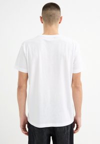 Camiseta blanca de manga corta con escote redondo, fabricada en algodón. Presenta un corte relajado y una textura suave, sin patrones ni acentos visibles.