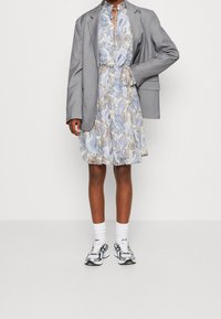 Blazer gris sur une robe paisley bleu clair, complété par des chaussettes blanches et des baskets argentées. La robe présente une taille cintrée et un motif floral.