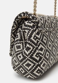 Black and white woven handbag with geometric diamond pattern and gold-tone twisted chain strap, angled side view.