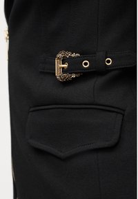 Μαύρο ύφασμα με μια τσέπη και μια περίτεχνη αγκράφα σε χρυσό τόνο, προσαρτημένη σε μαύρο λουρί που ταιριάζει.