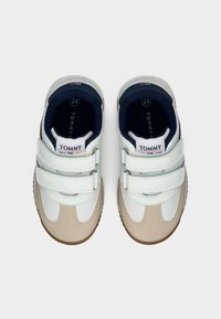 Λευκά και μπεζ παιδικά αθλητικά παπούτσια με λουράκια βέλκρο, εσωτερικό σε ναυτικό μπλε και λαστιχένια σόλα. Διαθέτουν ελαφριά υφή και ετικέτα «TOMMY» στη γλώσσα.