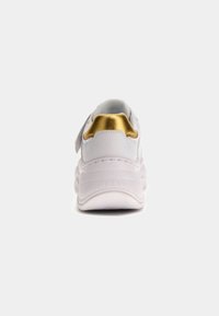 Białe, masywne sneakersy z złotą pętelką na pięcie, grubą podeszwą, i z wytłoczonym napisem "GUESS" z tyłu, pokazane od tyłu na jednolitym tle.