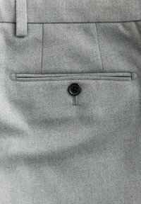 Pantalones de tela gris con un bolsillo trasero y un cierre de botón negro. La textura es suave con un patrón sutil.