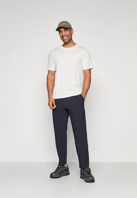 Camiseta blanca de manga corta, pantalones azul marino, gorra gris, zapatillas negras. Conjunto casual; tela suave, ajuste relajado y diseño práctico.
