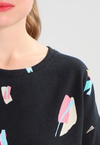 Zwarte trui met ronde hals, voorzien van abstracte patronen in roze, lichtblauw en crème. Zacht, gestructureerd stof, met een licht losse pasvorm.