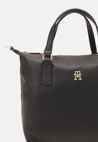 Zwarte leren handtas met twee bovenhandvatten, gouden metalen hardware en reliëflogo. Glad textuur en gestructureerd ontwerp met ritssluiting.