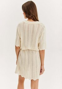 Sukienka dzianinowa z krótkim rękawem w kolorze kremowym, z teksturowanym wzorem, falbaniastym dołem i luźnym krojem z podkreśloną talią.