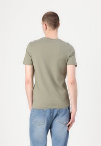 Ελιάς πράσινη, κοντομάνικη μπλούζα φτιαγμένη από βαμβάκι, με στρογγυλή λαιμόκοψη και εφαρμοστό σχήμα. Συνδυάζεται με ανοιχτό μπλε τζιν παντελόνι.