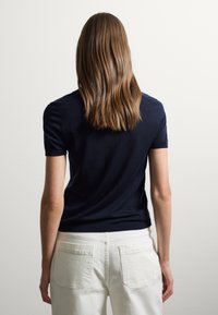 Maglietta a maniche corte blu navy con un design aderente. Indossata con pantaloni bianchi con tasche applicate. Tessuto morbido, dettagli a costine sui polsini e sull'orlo.