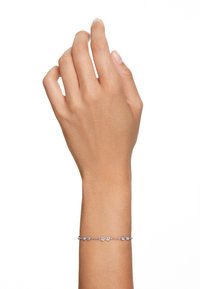 Srebrna bransoletka łańcuszkowa z okrągłymi i owalnymi akcentami, zdobiona przezroczystymi kamieniami przeplatanymi wzdłuż długości, noszona na dłoni.