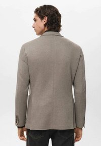 Blazer grigio textured con rever a punta, chiusura con un solo bottone e maniche lunghe. Presenta dettagli con bottoni ai polsini e una vestibilità sagomata.