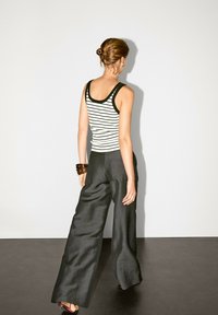 Stribet tank top i sort og hvid med mørk kant, parret med mørke vide bukser. Tilbehøret inkluderer et brunt bangle-armbånd. Minimalistisk baggrund.
