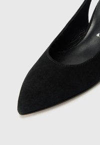 Scarpa nera in suede con tacco alto, punta affusolata e design con ritagli. Rivestimento interno liscio e dettagli di cucitura minimi.