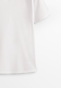 T-shirt blanc à manches courtes et col rond avec un tissu uni, présenté en plan rapproché de la poitrine vers le bas sur un fond clair.