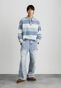 Denim öltözet, amely egy világoskék csíkos, galléros hosszú ujjú ingből és kopott, világos mosású bő nadrágból áll, amit barna cipők egészítenek ki.