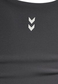 Sort træningstop med en glat, strækbar stof og lodret ribbning. To hvide chevron-grafikker er trykt på forsiden.