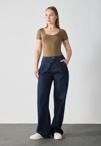 Brown fitted t-shirt paired with high-waisted, wide-leg dark denim jeans. White sneakers visible, simple design, and smooth texture.