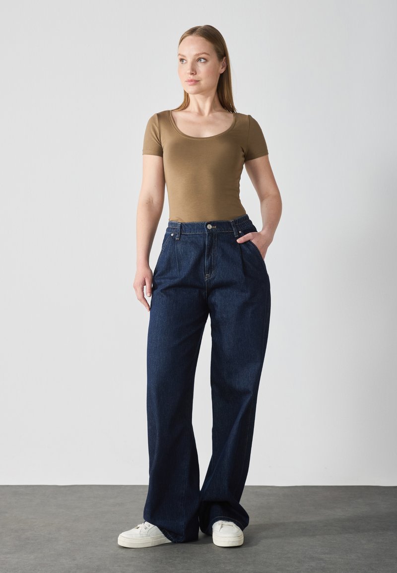 Brown fitted t-shirt paired with high-waisted, wide-leg dark denim jeans. White sneakers visible, simple design, and smooth texture.