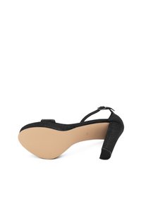 Scarpa nera con tacco a rocchetto, con tomaia testurizzata, punta aperta e tacco modesto. Presenta una suola beige liscia e una fascia decorativa.