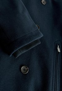 Marineblauer Wollmantel mit Knopfleiste, gerippten Bündchen und Reißverschlusstasche. Weicher Stoff mit glatter Textur und klassischem Design.