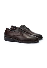 Chaussures en cuir marron avec une texture lisse, bout arrondi et design à lacets. Présente un petit logo en accent sur le côté et une semelle durable.