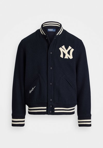 Casaco varsity de lã azul-marinho com colarinho e punhos em malha com riscas brancas, apresentando um logótipo NY bordado e uma assinatura na parte da frente.