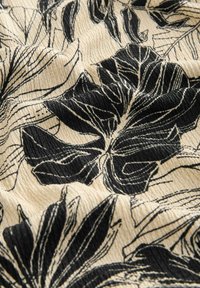 Svart- och vitt blommigt tyg med texturerad yta; har djärva bladmönster på en krämfärgad bakgrund, vilket skapar djup och kontrast.