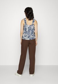 Top de alças com estampado floral em azul-marinho, com flores de tons claros, apresentando alças enveludadas. Combinado com calças largas castanhas e sapatilhas brancas.