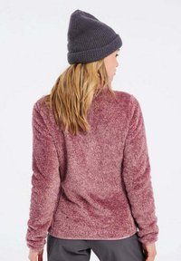 Pullover in polar fleece bordeaux con una superficie morbida e texturizzata e maniche lunghe, abbinato a un berretto a maglia grigio scuro. Presenta un collo rotondo.