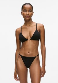 Melns bikini ar trīsstūrveida augšdaļu, plānām aizdares siksnām priekšpusē, un atbilstošām zema piegriezuma biksītēm ar šaurām sānu malām.