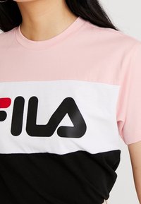 Camiseta de algodón de manga corta en rosa, blanca y negra con un audaz logo negro de "FILA" en el pecho. Diseño de color bloque sencillo.