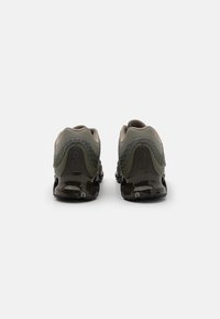 Dark green athletic shoes with a textured fabric upper, rounded shape, and glossy black rubber sole. Reinforced heel section and subtle logo detail.
