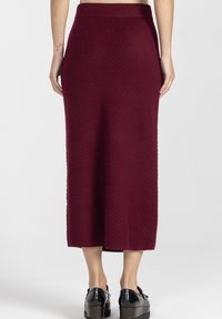 Bordowa dzianinowa spódnica midi w prążki z szerokim pasem, o prostym kroju i delikatnej fakturze, zestawiona z czarnymi butami na platformie.