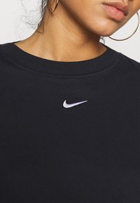 Svart sweatshirt med rund halsringning, tillverkad av mjukt tyg. Har en liten vit Nike-logotyp broderad på bröstet.